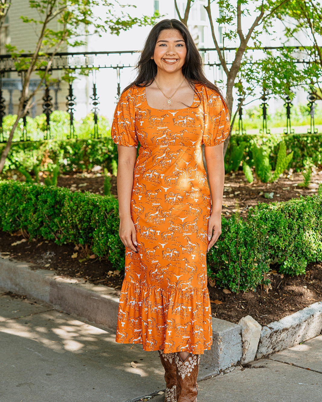 Woman wearing burnt orange Texas longhorn and horse patterned dress with ruffle bottom and puff sleeves