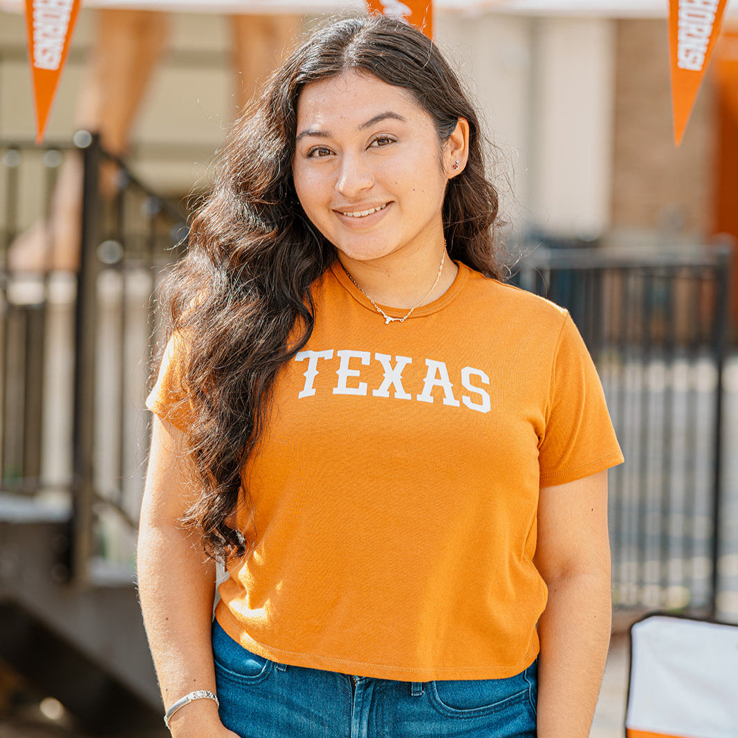 Woman wearing burnt orange cropped tee with Texas in a western font