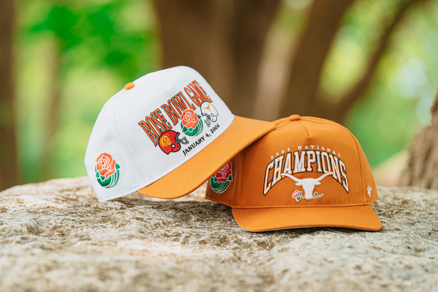 Two baseball caps, one white and one orange, with logos on a natural background.
