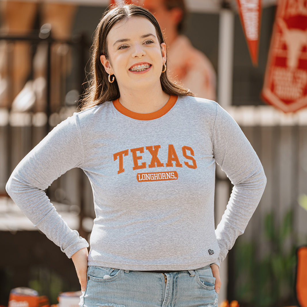 woman wearing grey longsleeve tee with burnt orange collar and burnt orange lettering that says Texas Longhorns