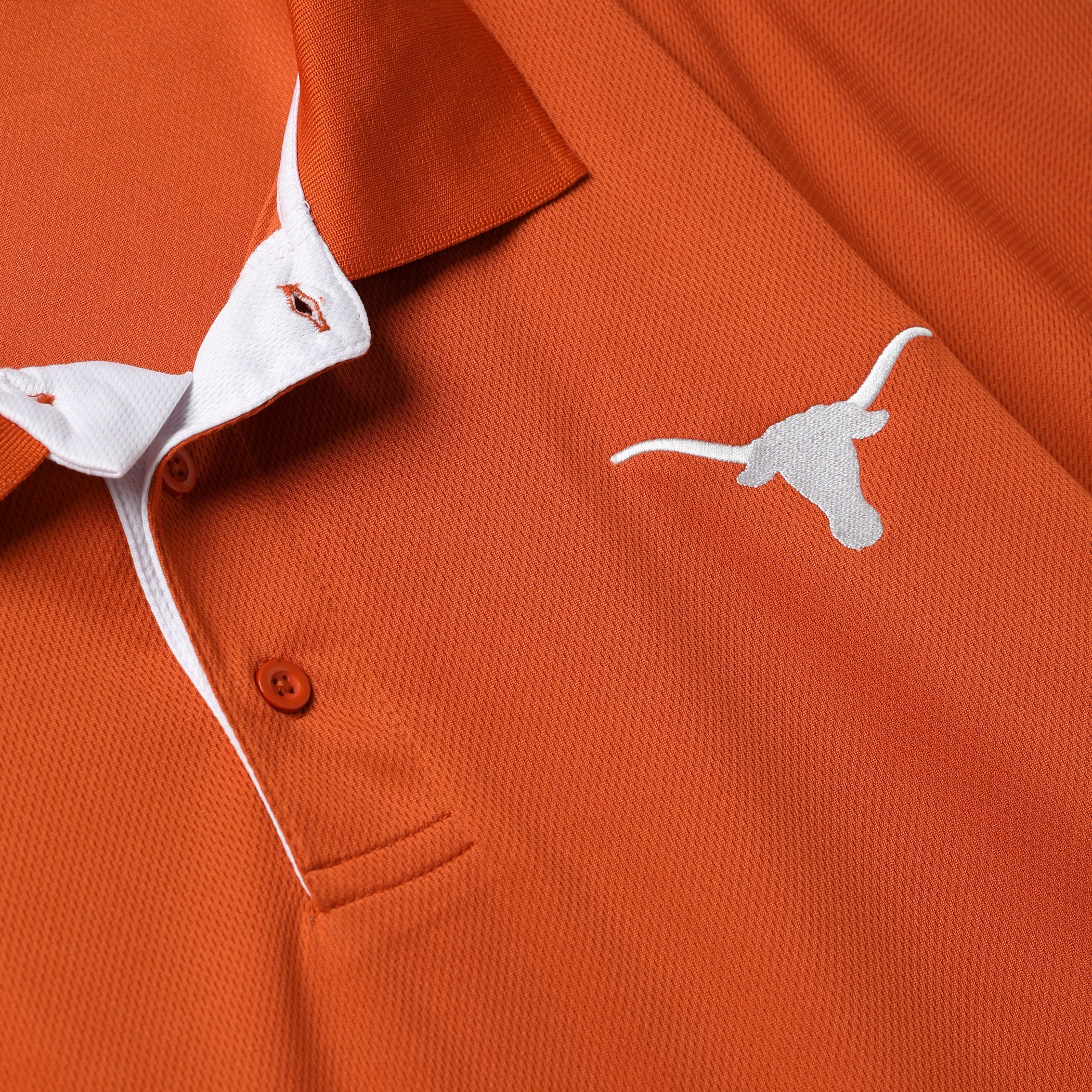 Close-up of an orange polo shirt with a white inner collar, orange buttons, and a white embroidered longhorn logo on the chest.