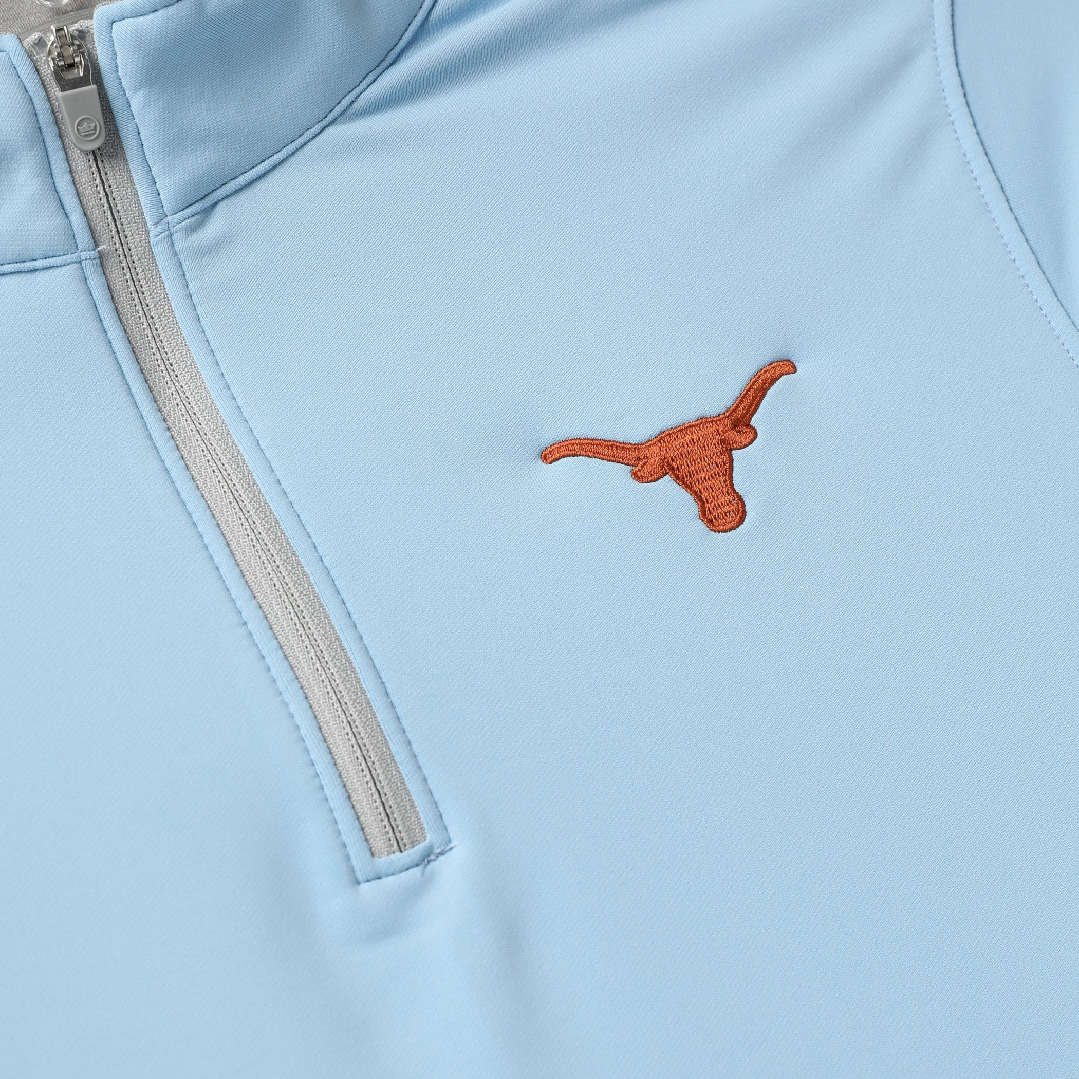 Close-up of a light blue half-zip jacket featuring an embroidered orange Texas Longhorns logo on the chest.