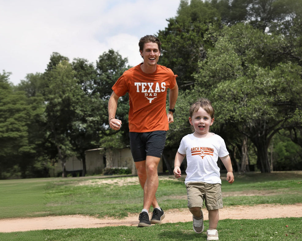 Man and child running together in a park with trees in the background