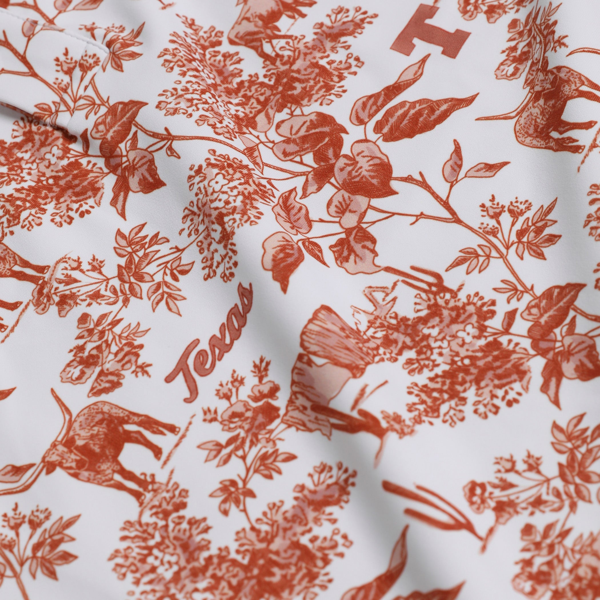 White fabric with a terracotta red toile-style print featuring deer, foliage, floral motifs, and the word Texas.