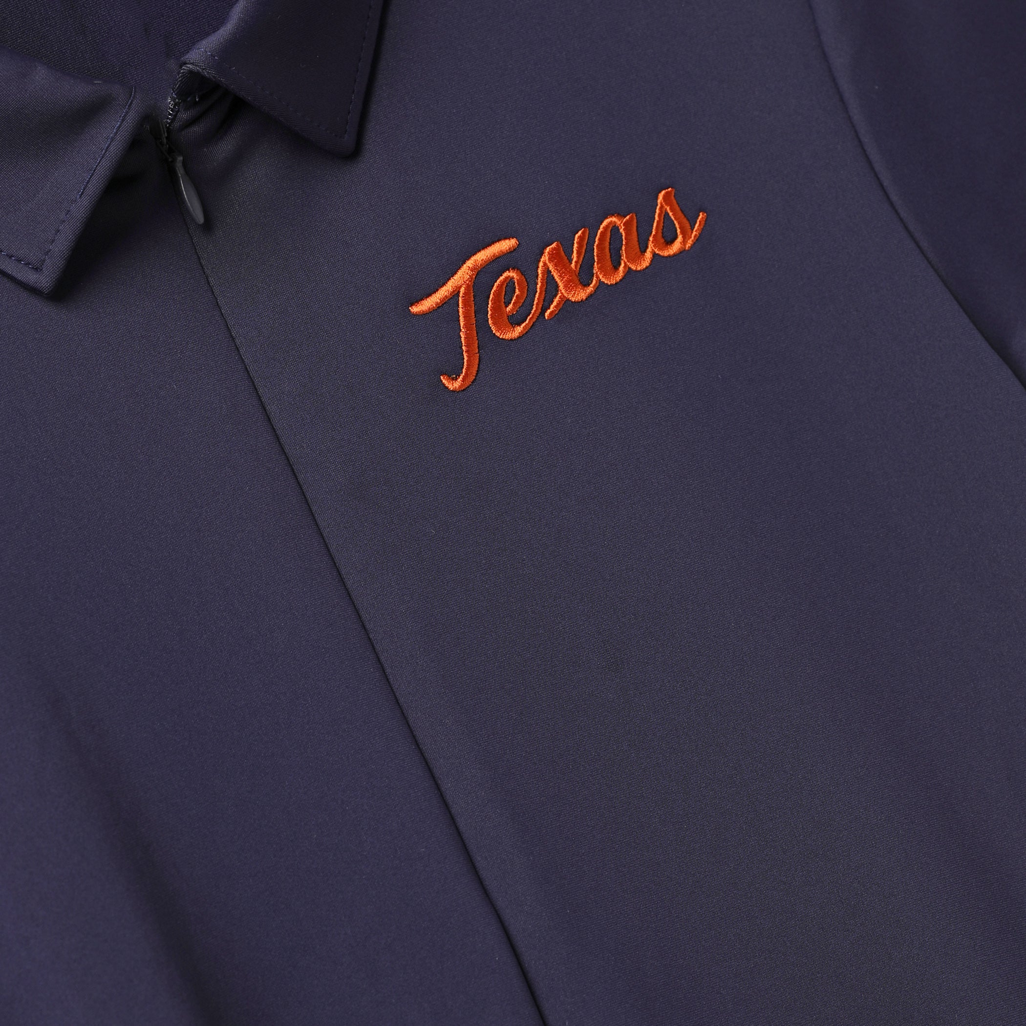 Close-up of a dark navy polo shirt with orange embroidered script reading 'Texas' on the chest.