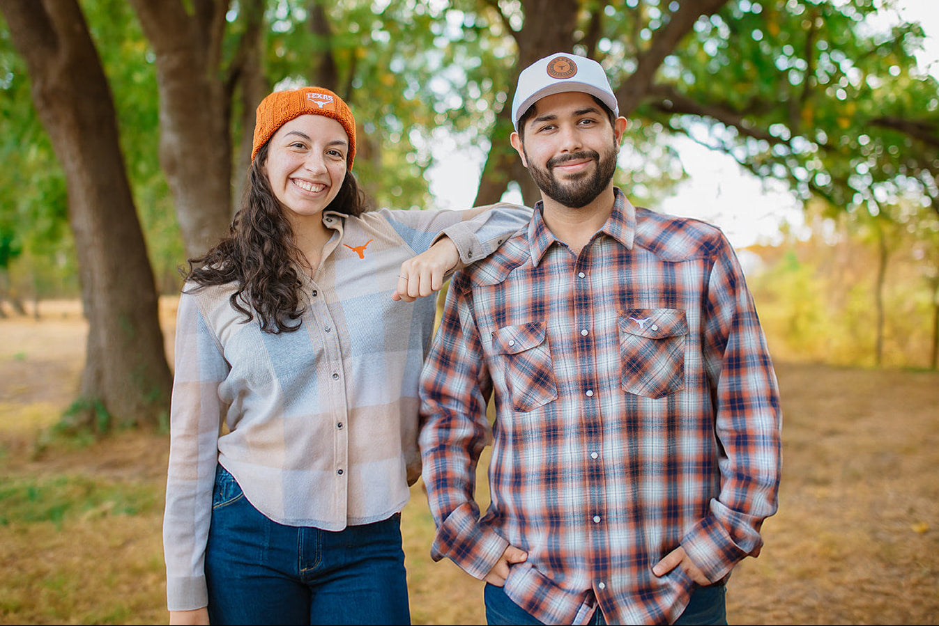 Two people standing outdoors in a natural setting with trees and grass.