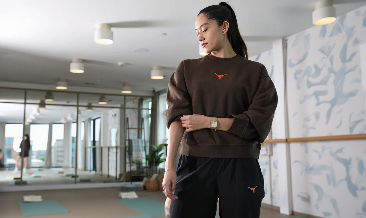 Woman wearing a brown sweatshirt with an orange logo in a modern indoor setting