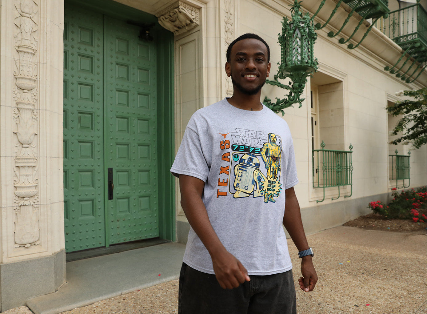 Man wearing a graphic t-shirt standing in front of a building with green doors.