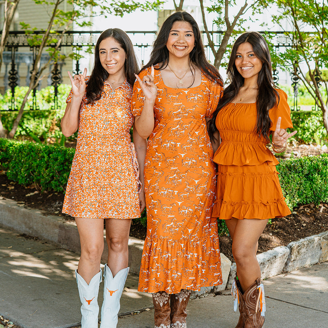 Women wearing burnt orange Texas Longhorns dresses with cowboy boots