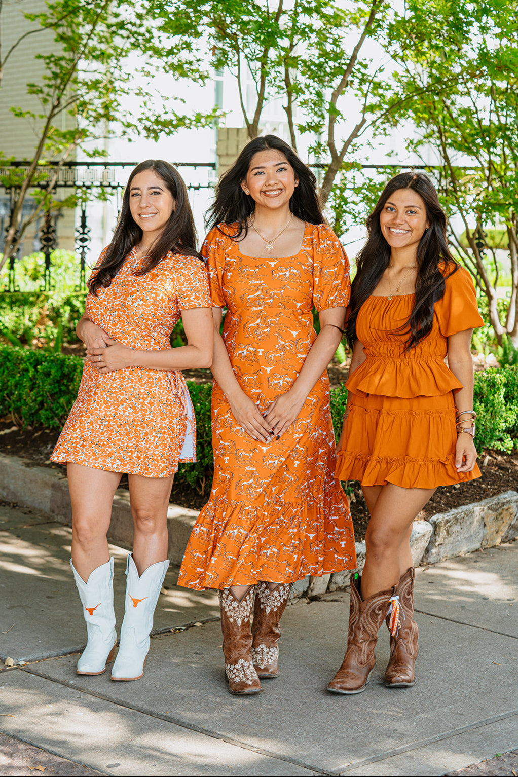 Longhorn women in orange dresses standing outdoors with trees in the background. Longhorn Tailgating in Fashion