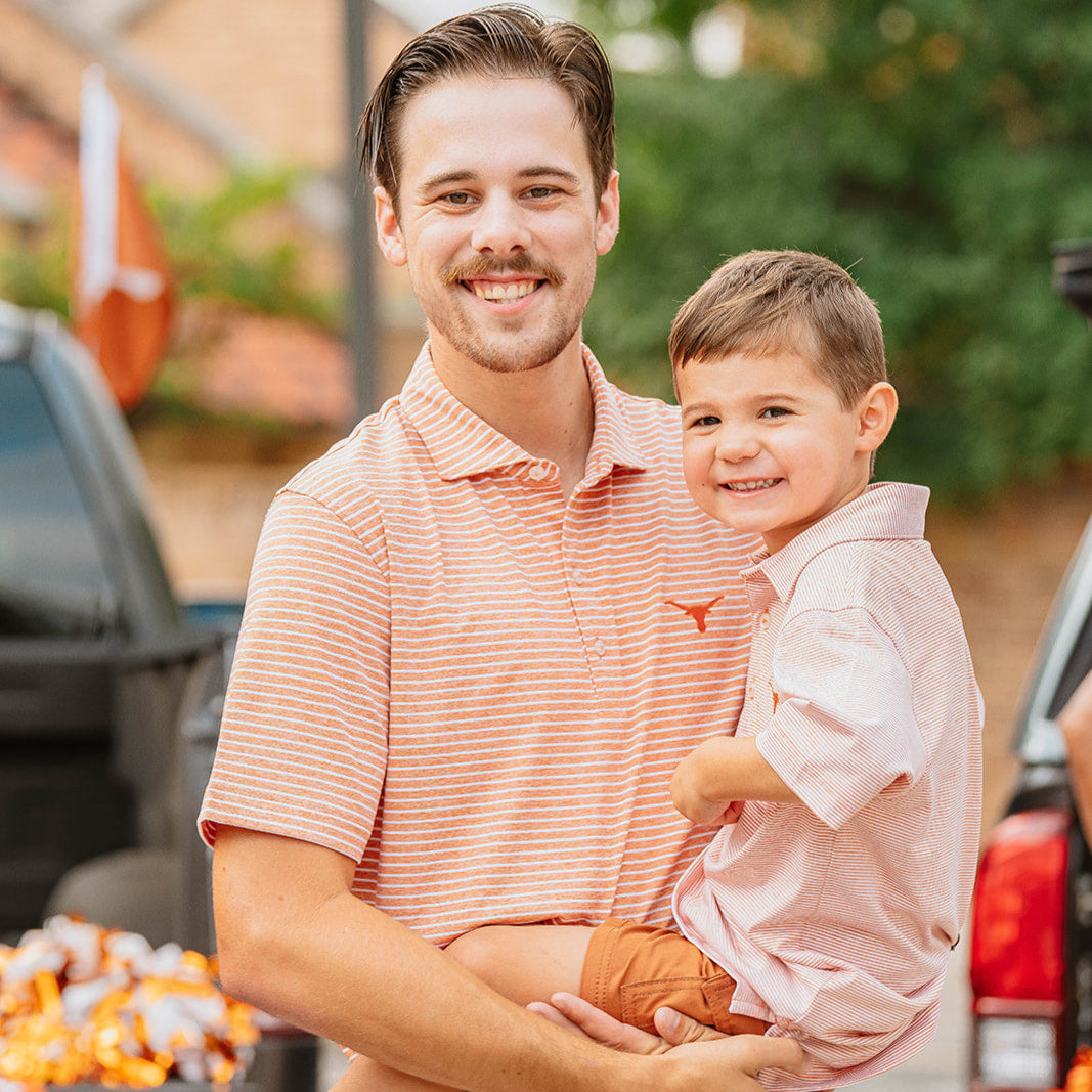 Man wearing burnt orange and white striped polo from Johnnie-O, holding toddler wearing a matching Longhorn Johnnie-O polo