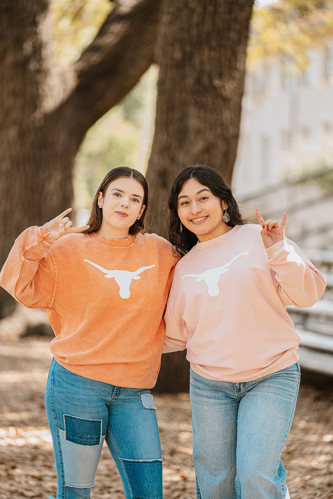 Two women wearing Texas Longhorns sweatshirts standing outdoors near a tree.