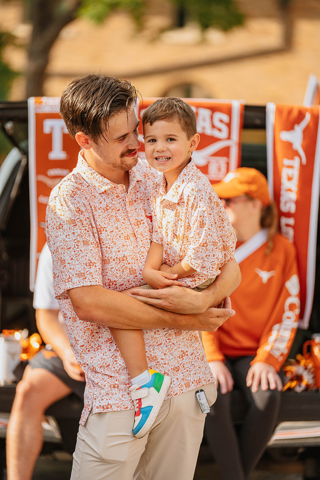 longhorn dad holding a child in front of Texas Longhorns banners. Tailgate longhorn merch