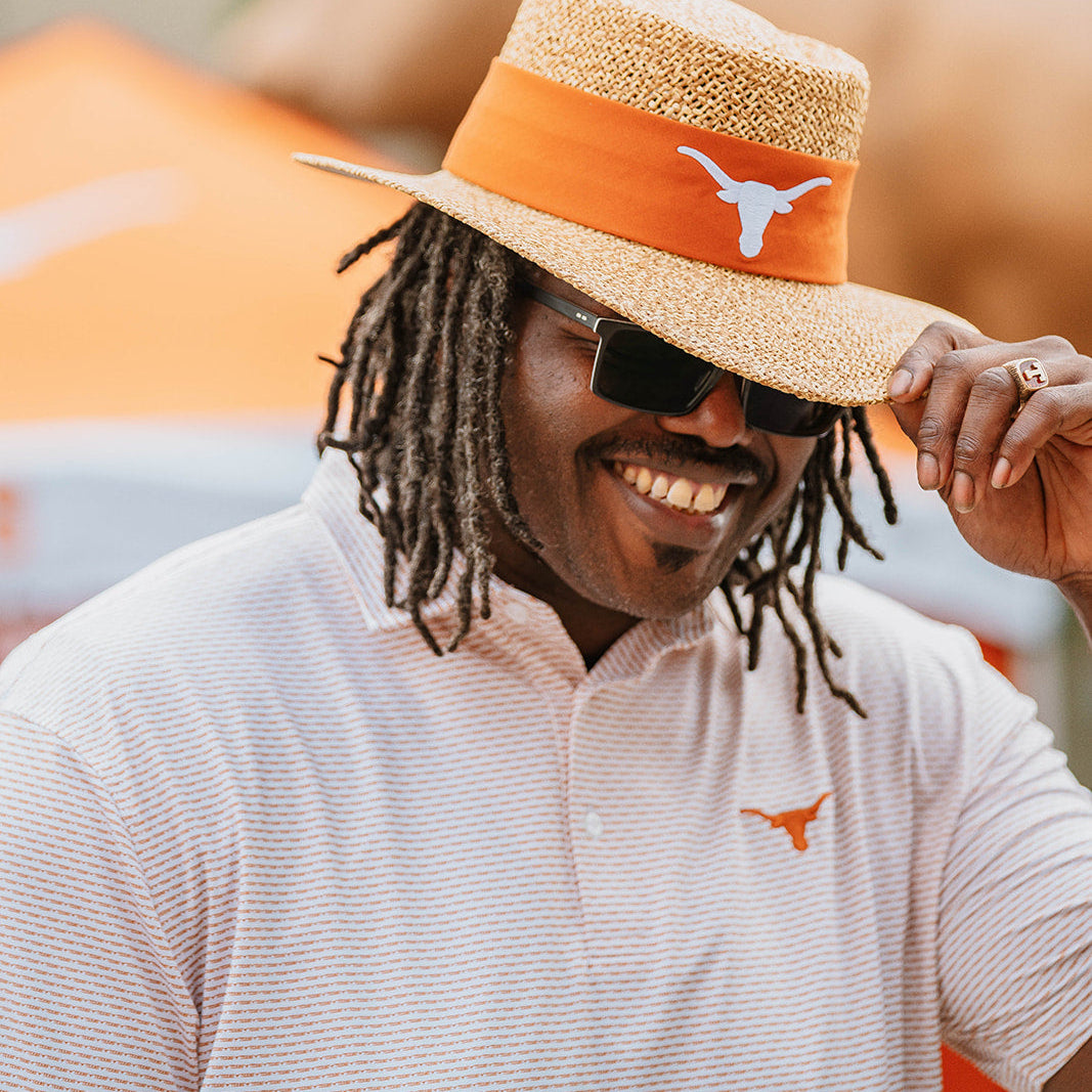 Man wearing white and burnt orange Texas Longhorns polo with a University of Texas straw hat