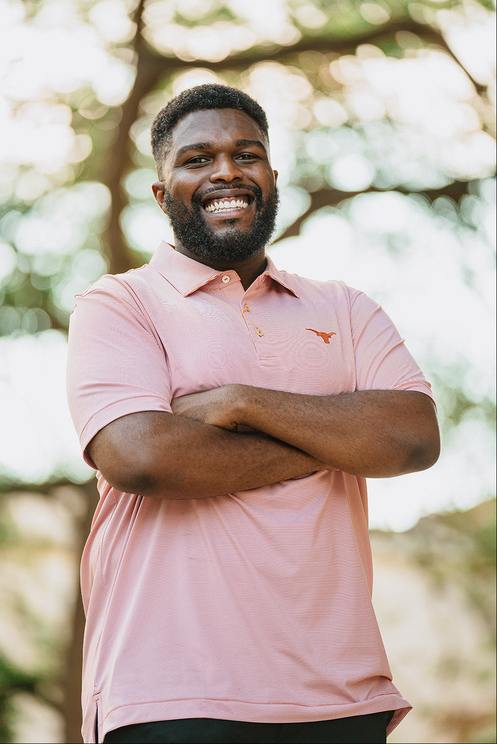 Man wearing a pink polo shirt with a blurred natural background