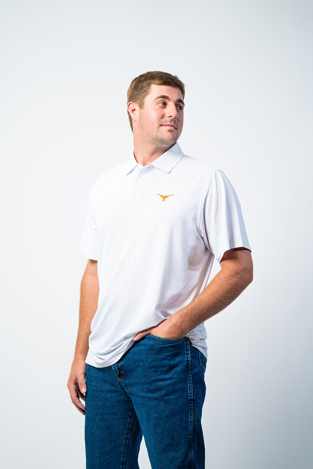Man wearing a white polo shirt with a logo on a plain background