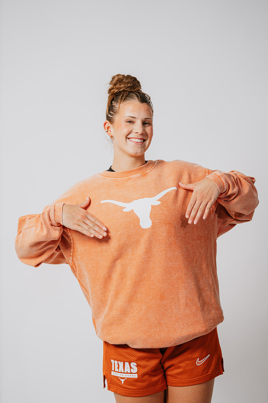 Texas Longhorns Basketball player wearing an orange sweatshirt with a logo and matching shorts on a plain background. Texas Longhorns merch