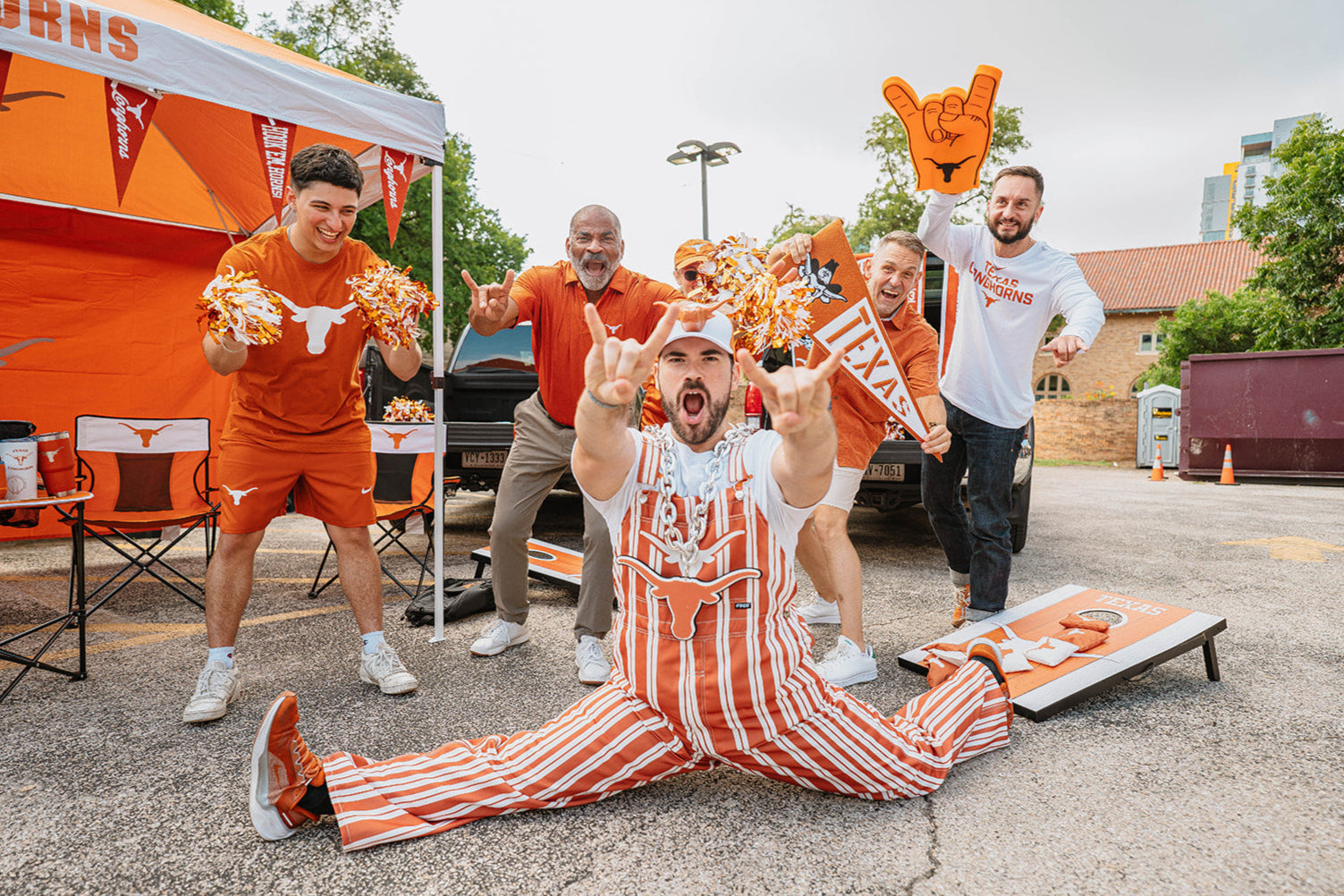 Group of longhorn fans celebrating outdoors with a man in a striped outfit sitting on the ground. Tailgate with longhorn merch