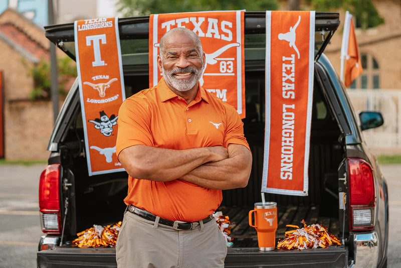 Man standing in front of a car trunk decorated with Texas Longhorns banners and tailgating food.
