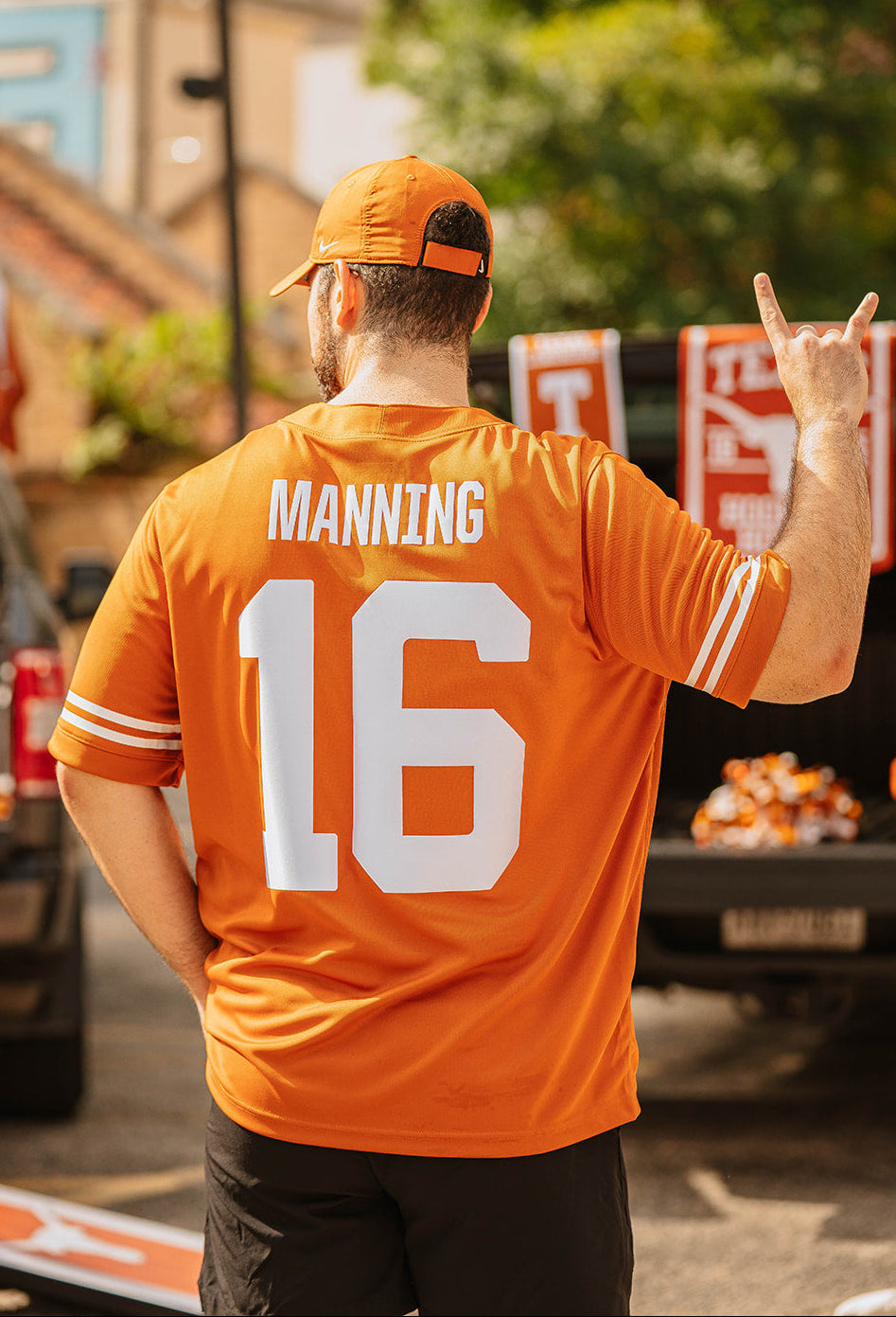 A man seen from behind wearing an orange Tennessee Titans jersey with 'MANNING' and the number '16' on the back, along with an orange cap, standing outdoors near a truck.