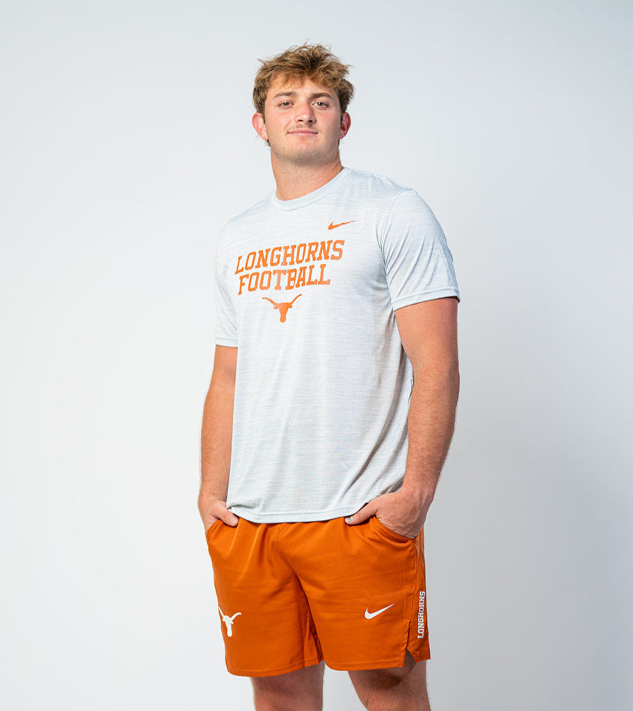 Person wearing a white t-shirt with 'Longhorns Football' text and orange shorts on a white background. Texas Longhorns merch