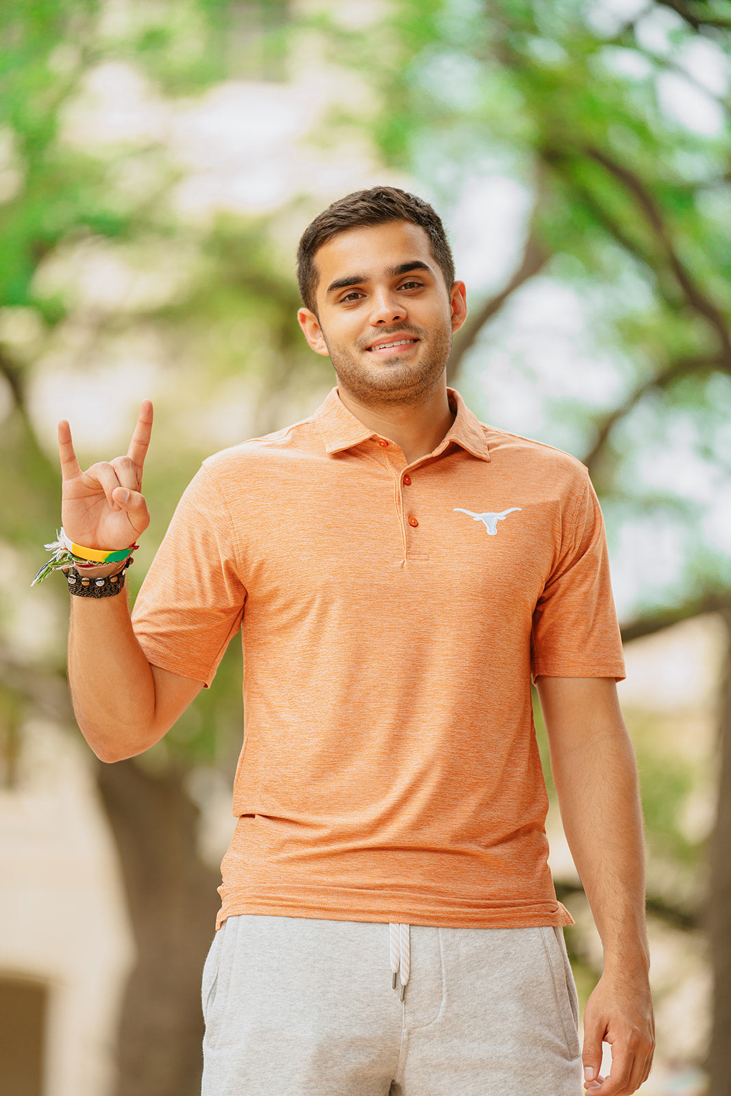 Man wearing an orange polo shirt with a logo, standing outdoors with trees in the background