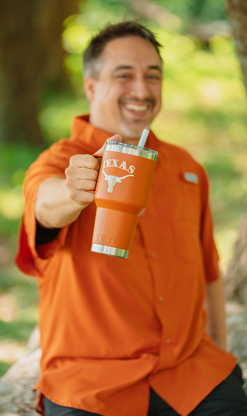 Man in orange shirt holding a Texas-themed tumbler outdoors