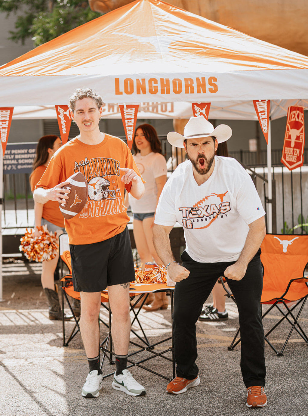 Two men in Texas-themed clothing under a 'Longhorns' umbrella at an outdoor event.