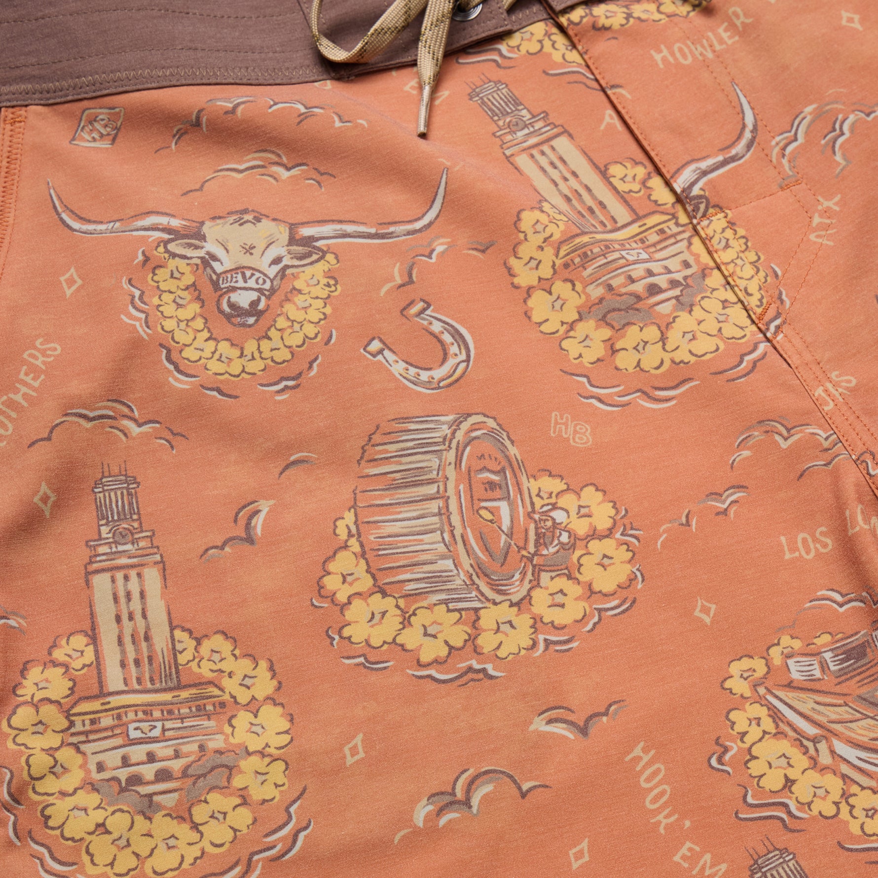 Close-up of peach-orange patterned fabric with a brown waistband and beige drawstring, featuring repeated illustrations of a longhorn steer head in a floral wreath, a tower, a horseshoe, a barrel, birds, and small text.