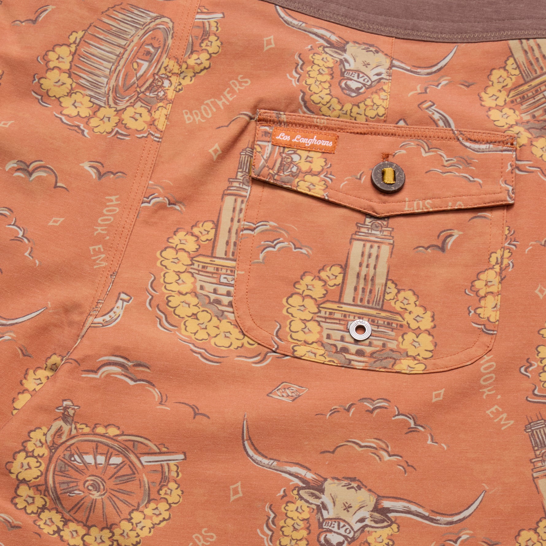 Close-up of a peach-orange denim garment featuring a printed graphic pattern with yellow flowers, a steer skull, a tower, and the text 'Los Angeles' and 'Hooch & En'. A front pocket with a button and a visible 'Los Angeles' tab is shown.