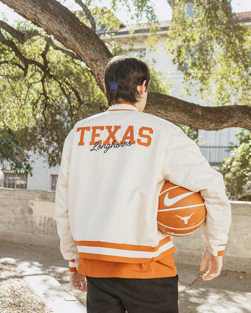 Person wearing a Texas-themed jacket and holding a basketball in an outdoor setting.
