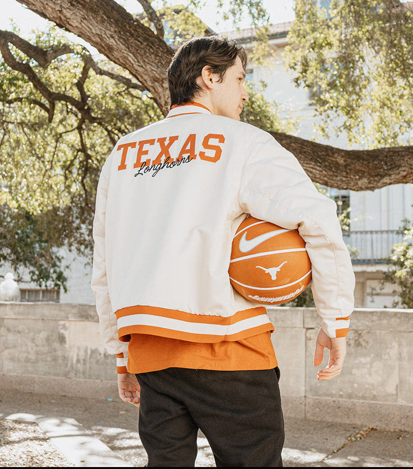 Person wearing a Texas-themed jacket holding a basketball outdoors.