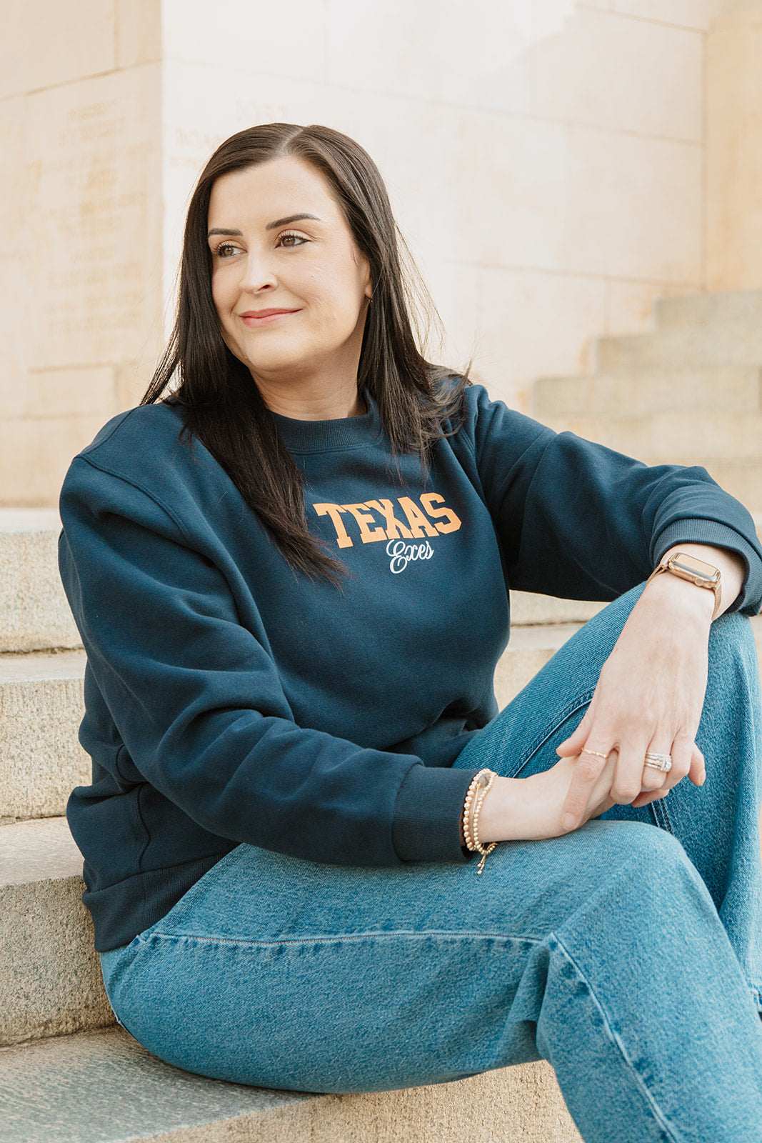 Woman wearing a blue sweatshirt with 'TEXAS' printed on it, sitting on steps.