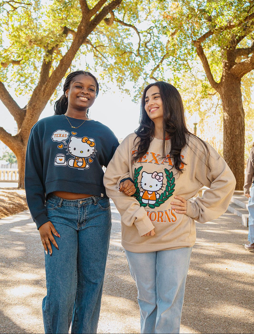 Two women wearing Hello Kitty-themed sweatshirts standing outdoors with trees in the background.