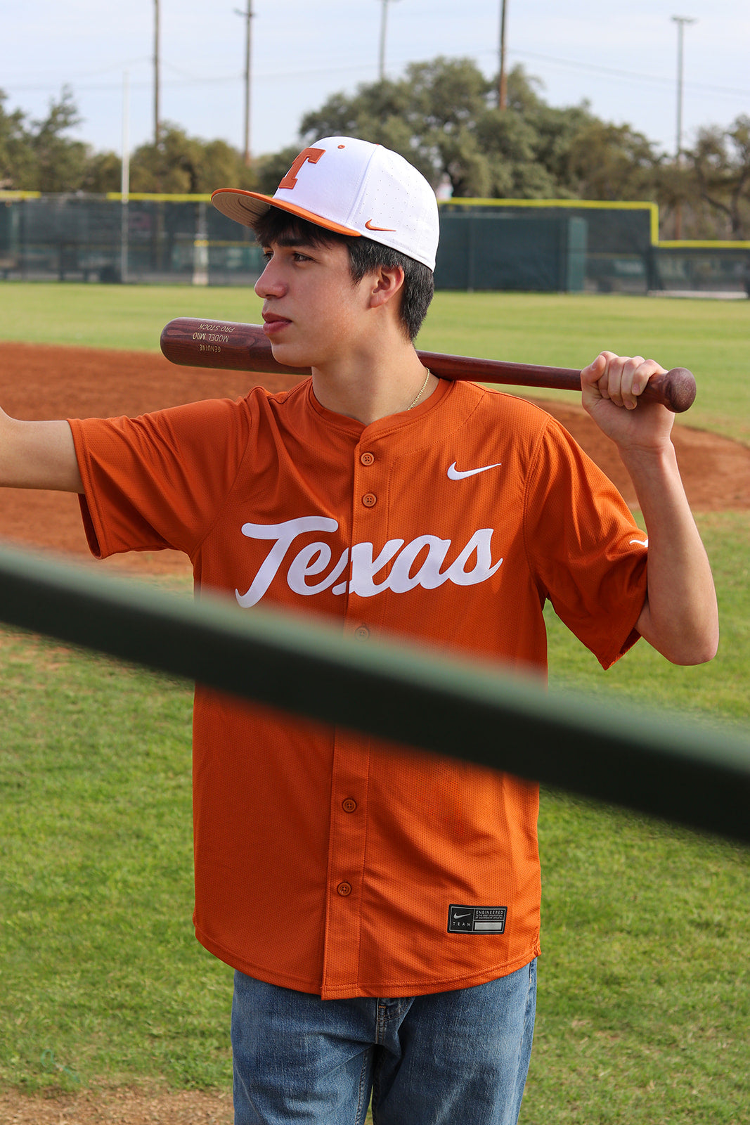 Person wearing an orange 'Texas' baseball jersey holding a bat on a baseball field.