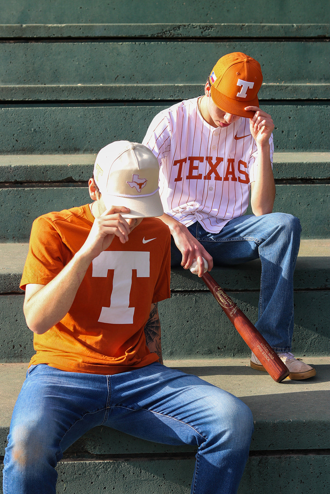 Two people sitting on bleachers wearing Texas-themed clothing and hats.