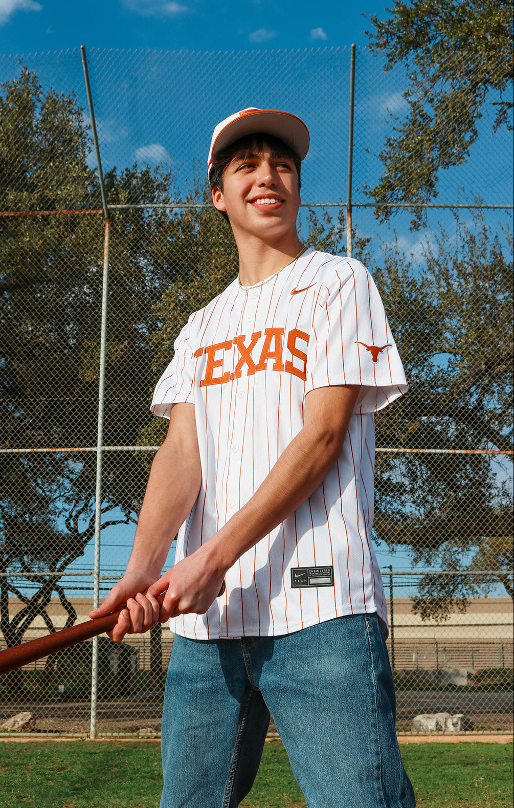 Person wearing a Texas-themed baseball jersey holding a bat on a sports field.