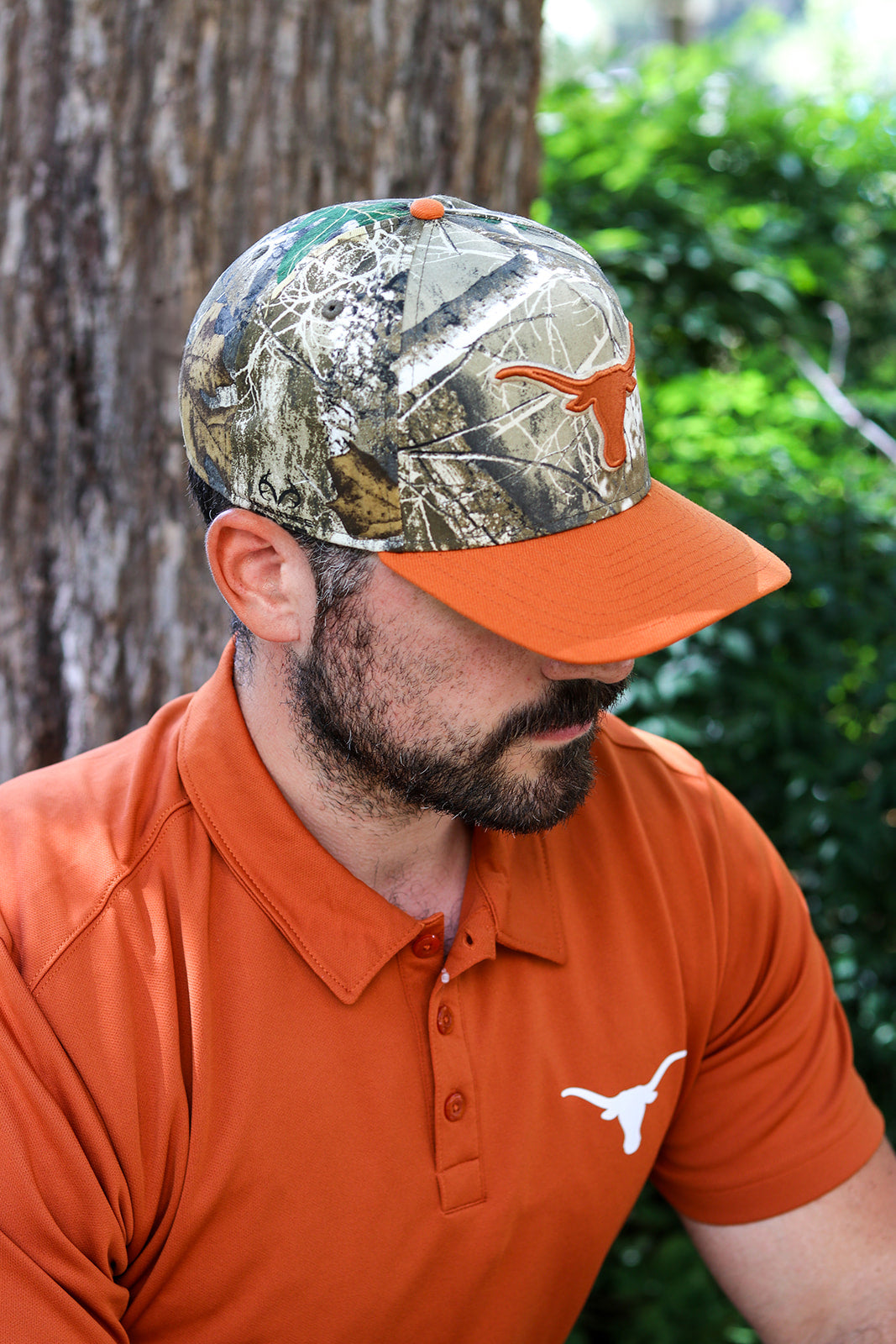 A man wearing a Texas Longhorns themed baseball cap with a Realtree camouflage pattern and an orange brim, paired with an orange polo shirt featuring the Texas Longhorns logo.
