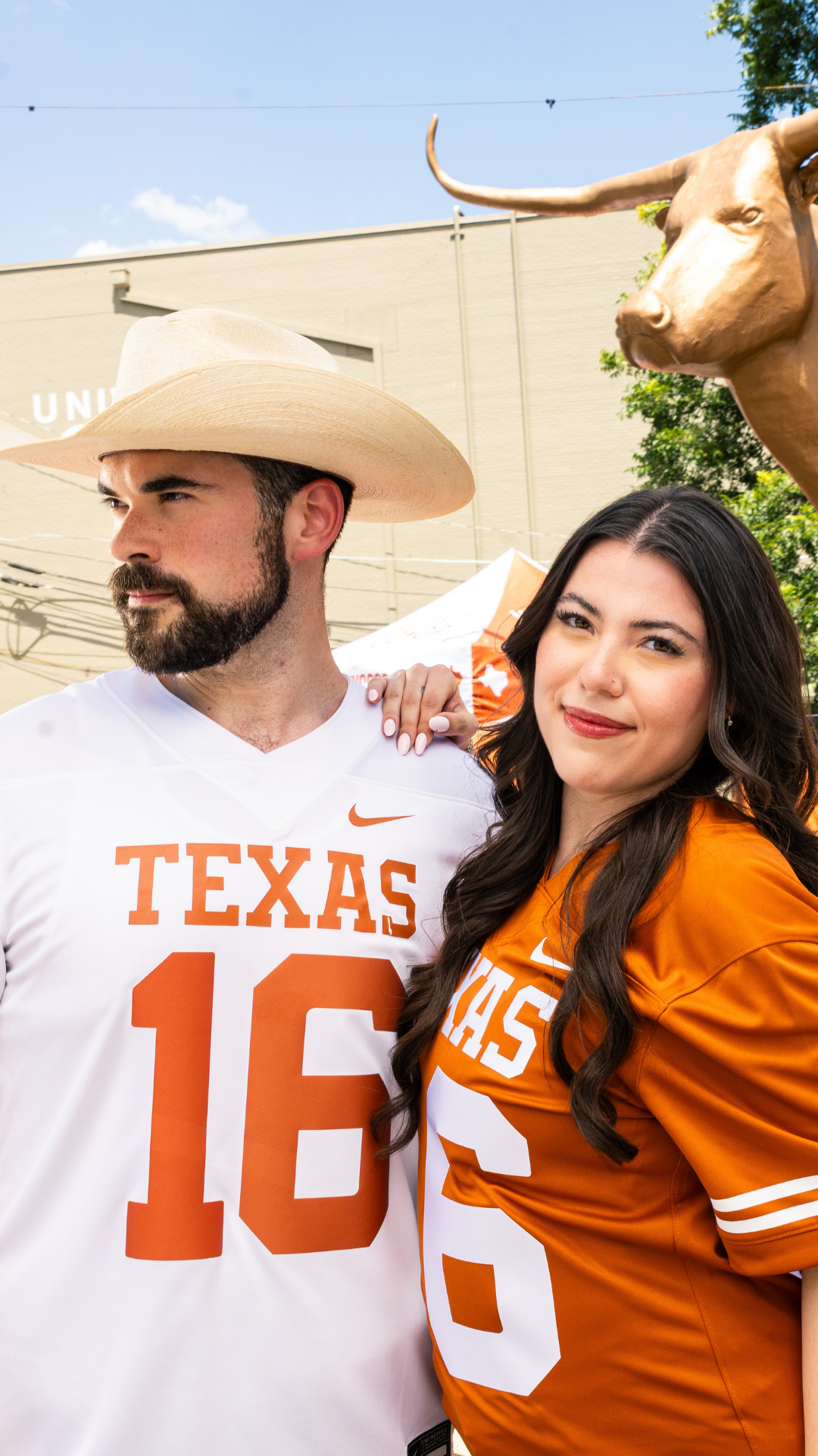 A man and a woman posing outdoors in Texas football jerseys. The man on the left wears a white jersey with orange lettering and number 16, paired with a beige cowboy hat.