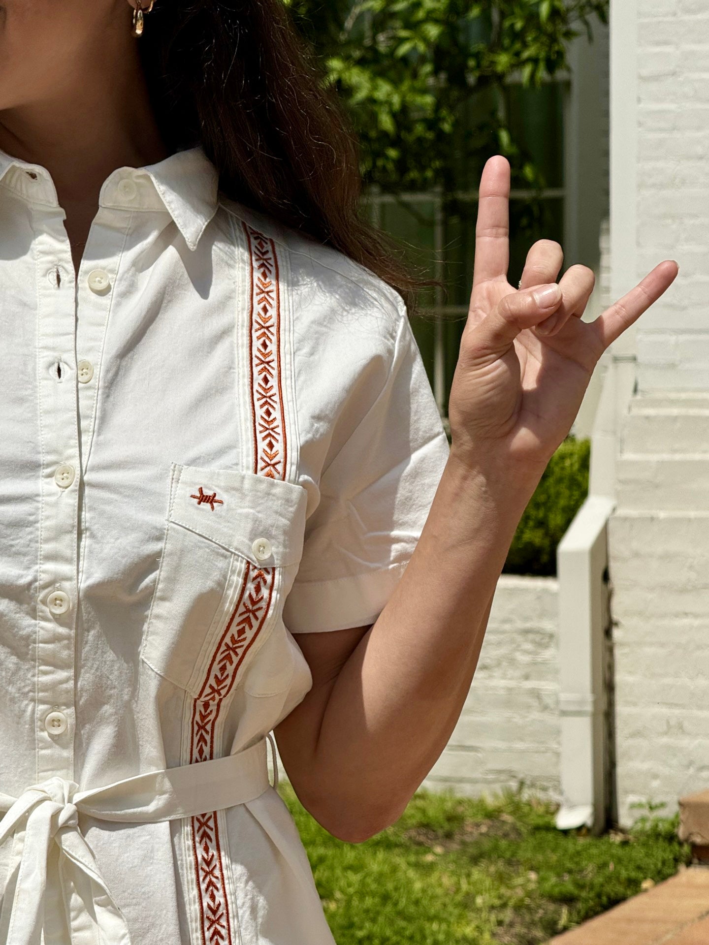 Woman wearing white Texas Standard dress with burnt orange stitching and hook 'em hand sign